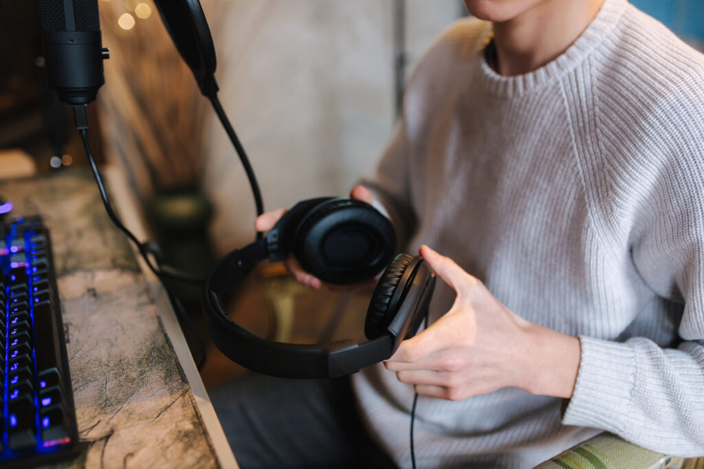 Closeup of man wearing headphones during the work with music at home. Background of micrphone and pc with keyboard. Neon light
