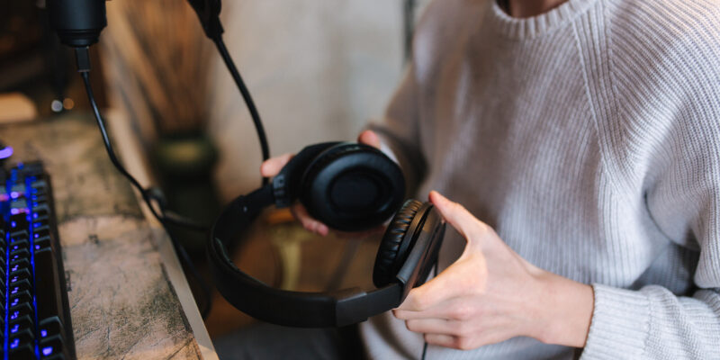 Closeup of man wearing headphones during the work with music at home. Background of micrphone and pc with keyboard. Neon light