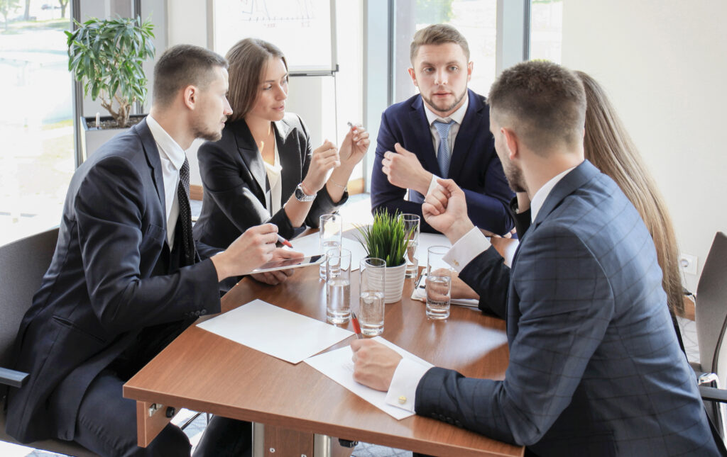 Young man discussing something while his coworkers listening to him sitting at the office table